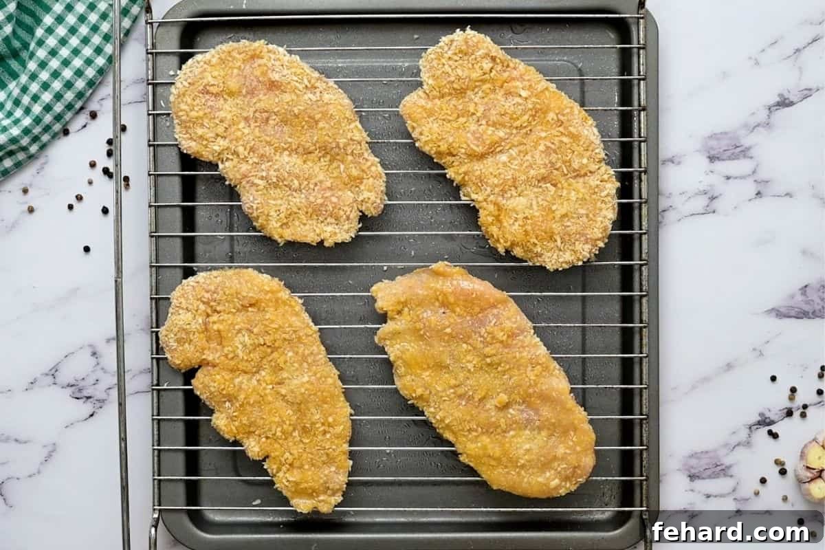 Perfectly breaded chicken cutlets arranged on a baking rack, ready for the oven.
