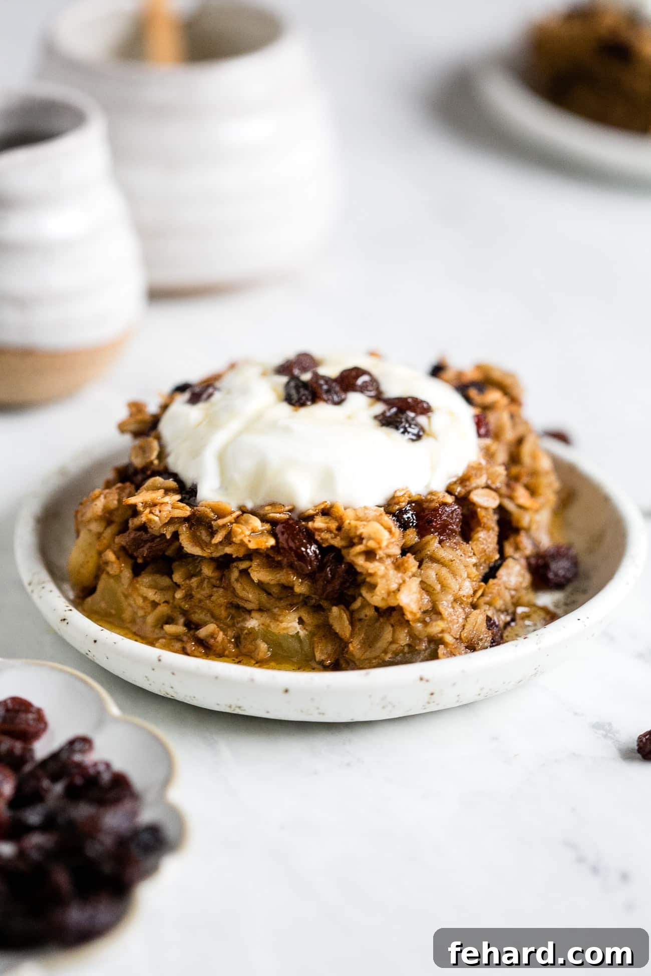Comforting Apple Raisin Oatmeal Bake 2 A perfectly portioned slice of warm Apple & Raisin Baked Oatmeal, elegantly topped with a dollop of creamy Greek yogurt and a sprinkle of fresh cinnamon.