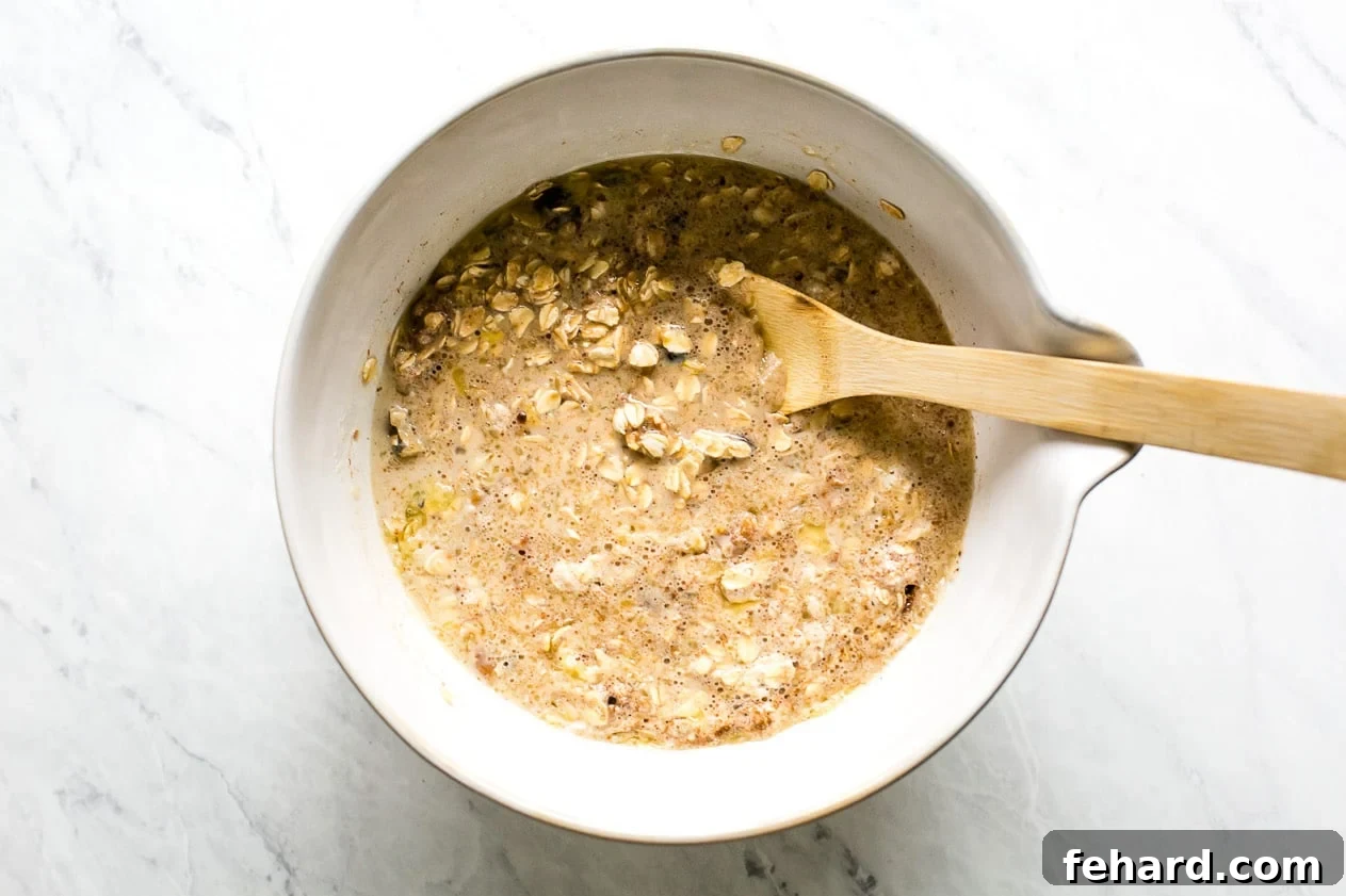 Comforting Apple Raisin Oatmeal Bake 7 The wet and dry ingredients for baked oatmeal are thoroughly combined in a large mixing bowl, forming a thick, uniform batter speckled with oats, raisins, and walnuts.