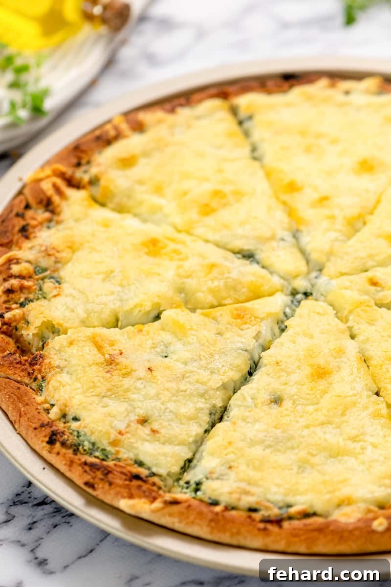 Spinach Pizza made with Ricotta Close up of spinach pizza sliced into 8 wedges, showcasing the creamy white sauce, green spinach, and melted cheese.