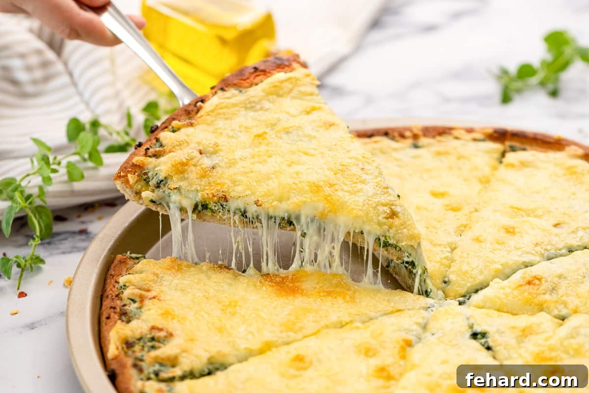 Spinach White Pizza Slice of spinach pizza being pulled out from pizza tray, showing the set cheese and toppings.