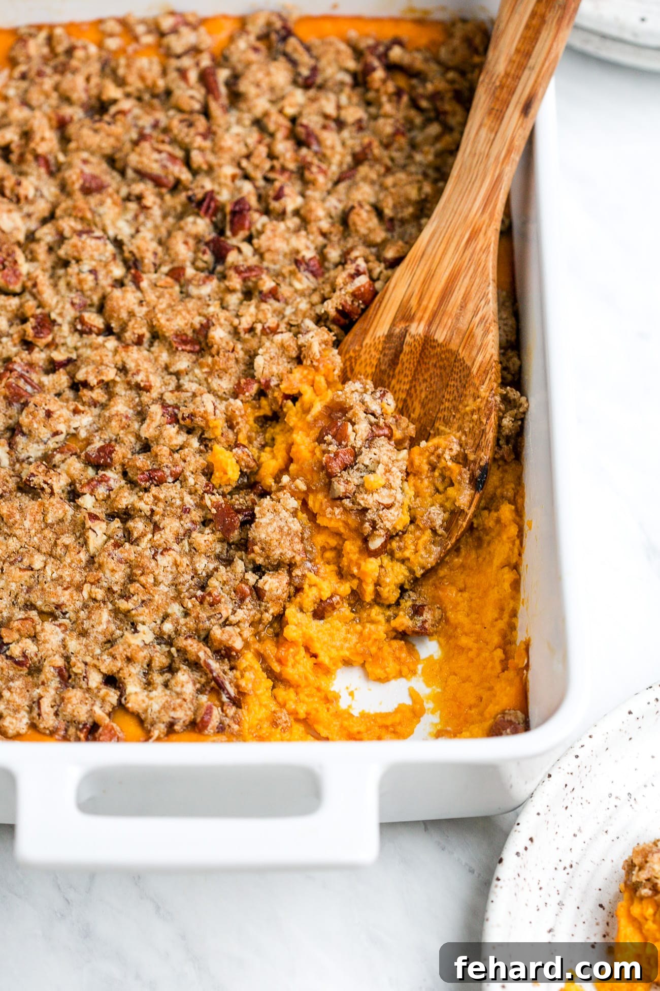 Close-up of a serving of baked sweet potato casserole, revealing its creamy interior and crunchy, golden pecan streusel topping, scooped onto a plate.