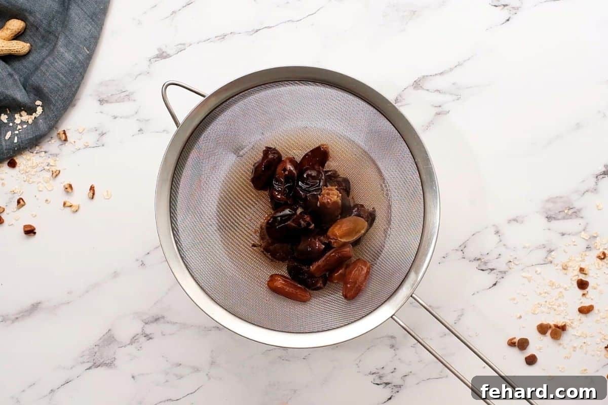 Softened Dates for Granola Bar Recipe Pitted dates soaking in a mesh colander after being steeped in hot water, looking plump and ready for processing into a smooth paste.