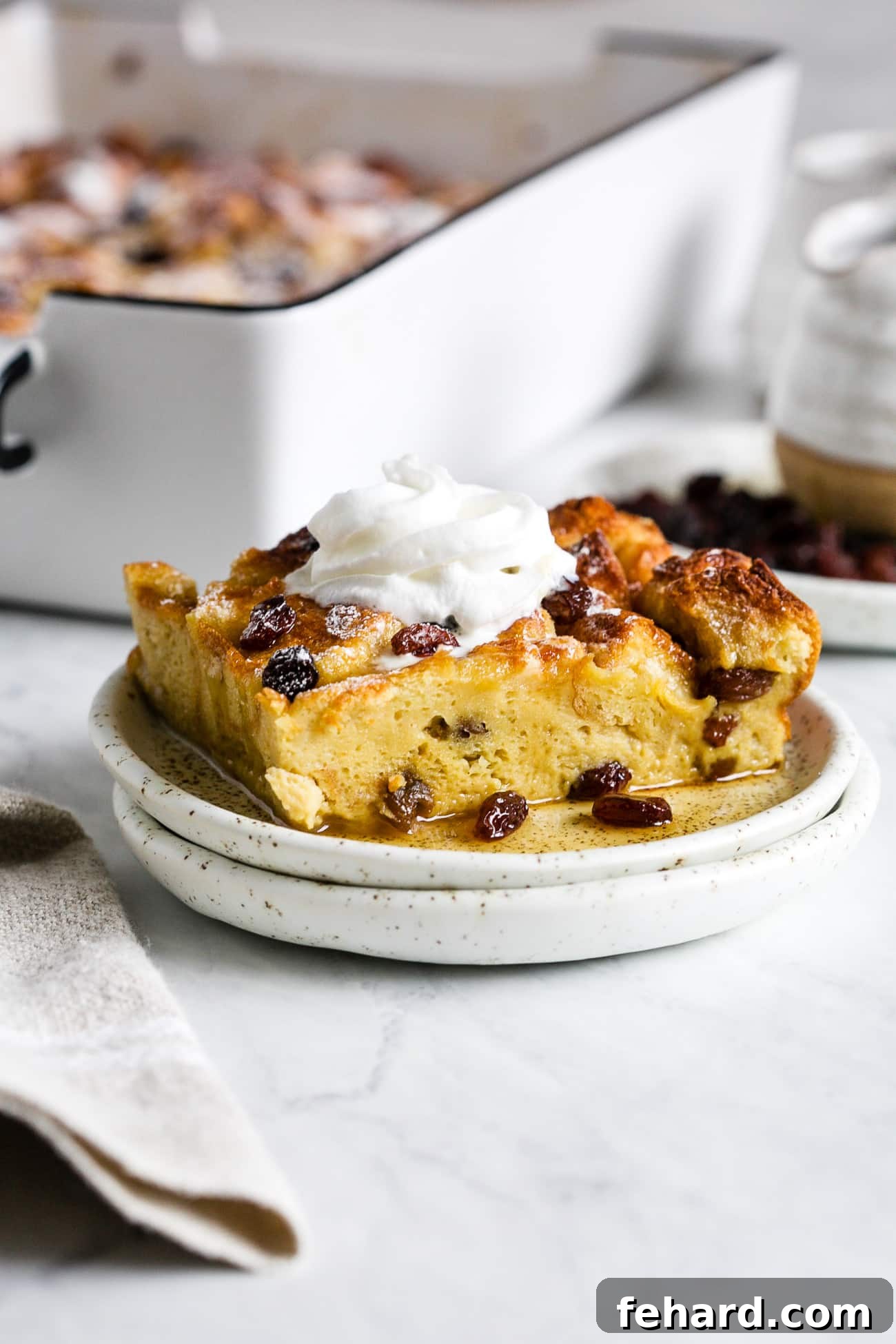 A delectable slice of French toast casserole, golden brown with a dusting of powdered sugar and a dollop of whipped cream, served on a white plate.