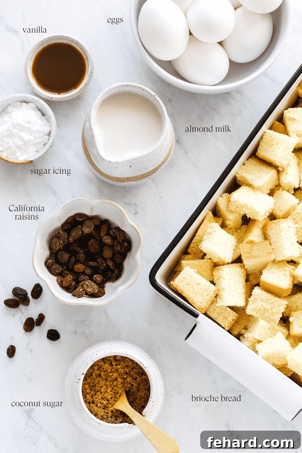 An artfully arranged collection of key ingredients for French toast casserole, including bread, eggs, milk, sugar, and raisins, laid out on a clean white countertop.
