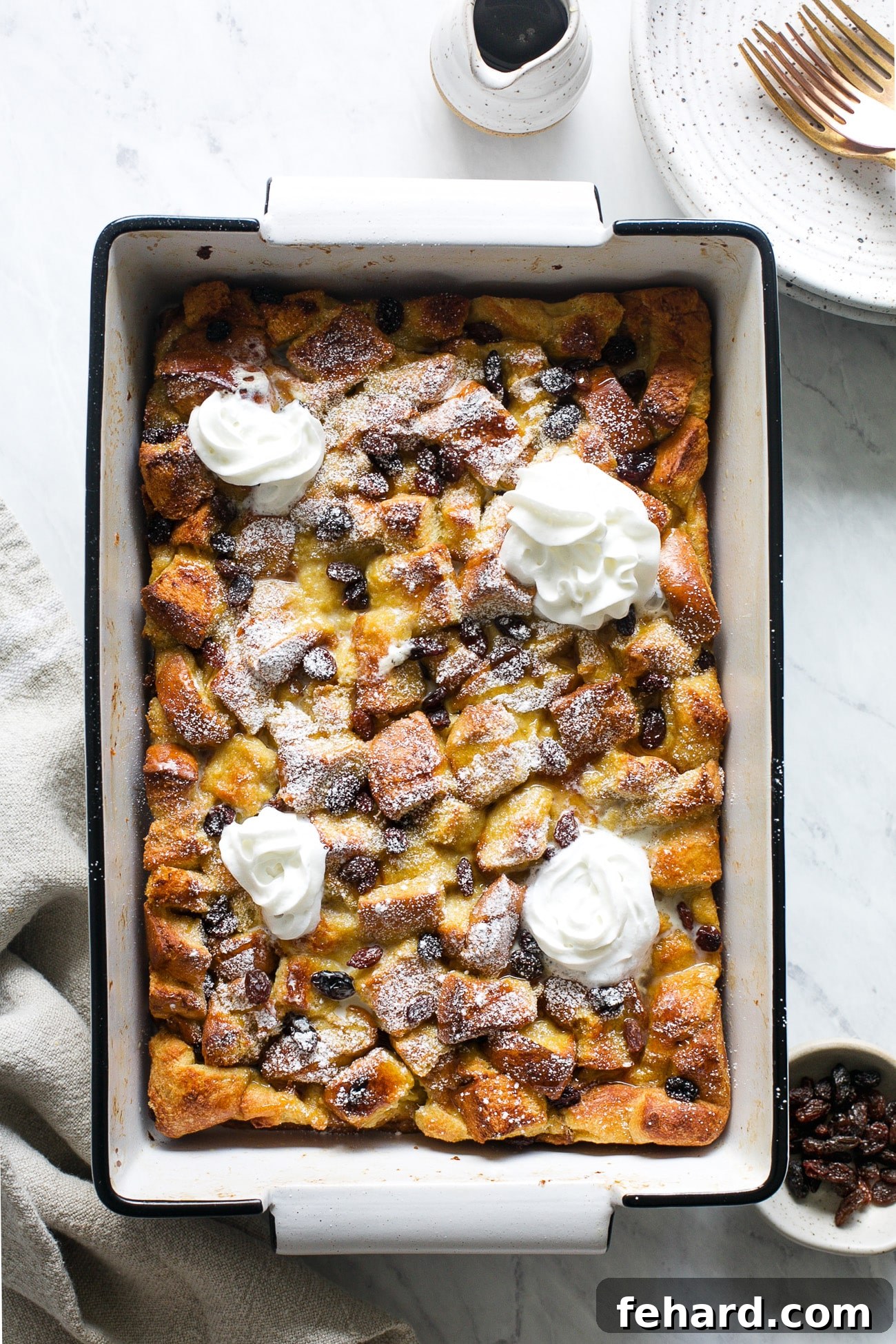 A beautifully golden-brown French toast casserole, fresh out of the oven, topped with a generous swirl of whipped cream and a dusting of powdered sugar.