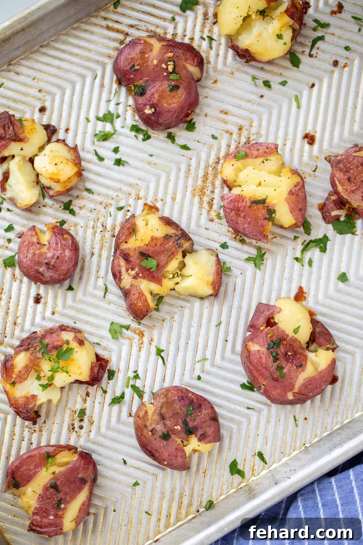 Crispy smashed potatoes on a sheet pan, garnished with fresh parsley.
