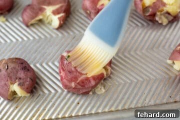 A pastry brush applying garlic butter over smashed potatoes on a sheet pan.