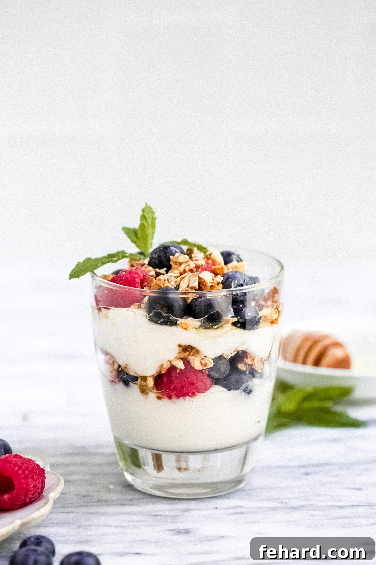 Closeup view of a freshly made yogurt parfait in a clear glass, showing distinct layers of yogurt, berries, and granola.