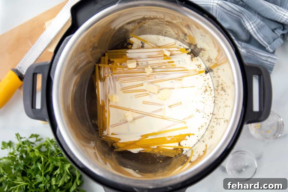 Layering Noodles in Instant Pot Alfredo Fettuccine noodles arranged in a criss-cross pattern in the Instant Pot inner pot, topped with cream and butter.