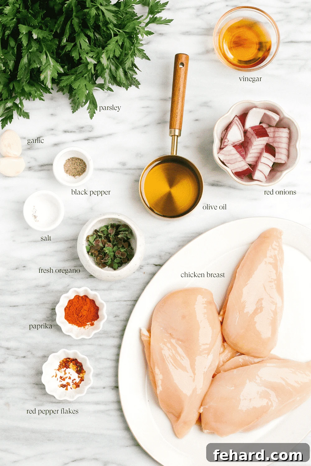 A selection of fresh ingredients including herbs, garlic, and oil, neatly arranged on a marble board, ready to make grilled chicken chimichurri.