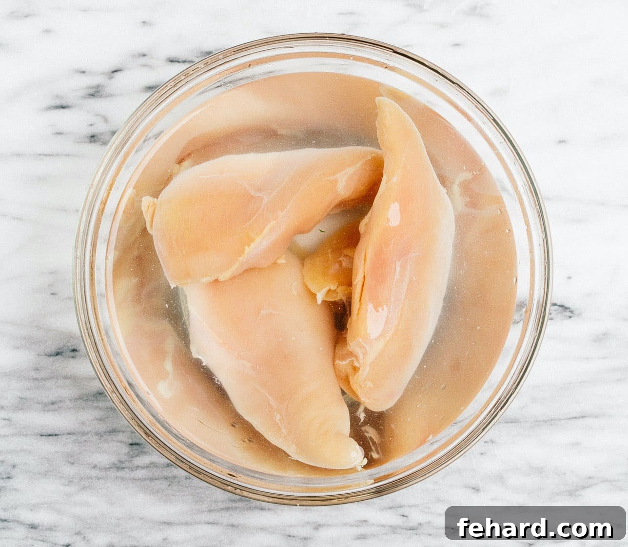 Raw chicken breasts soaking in a bowl of water and salt, indicating the brining process.