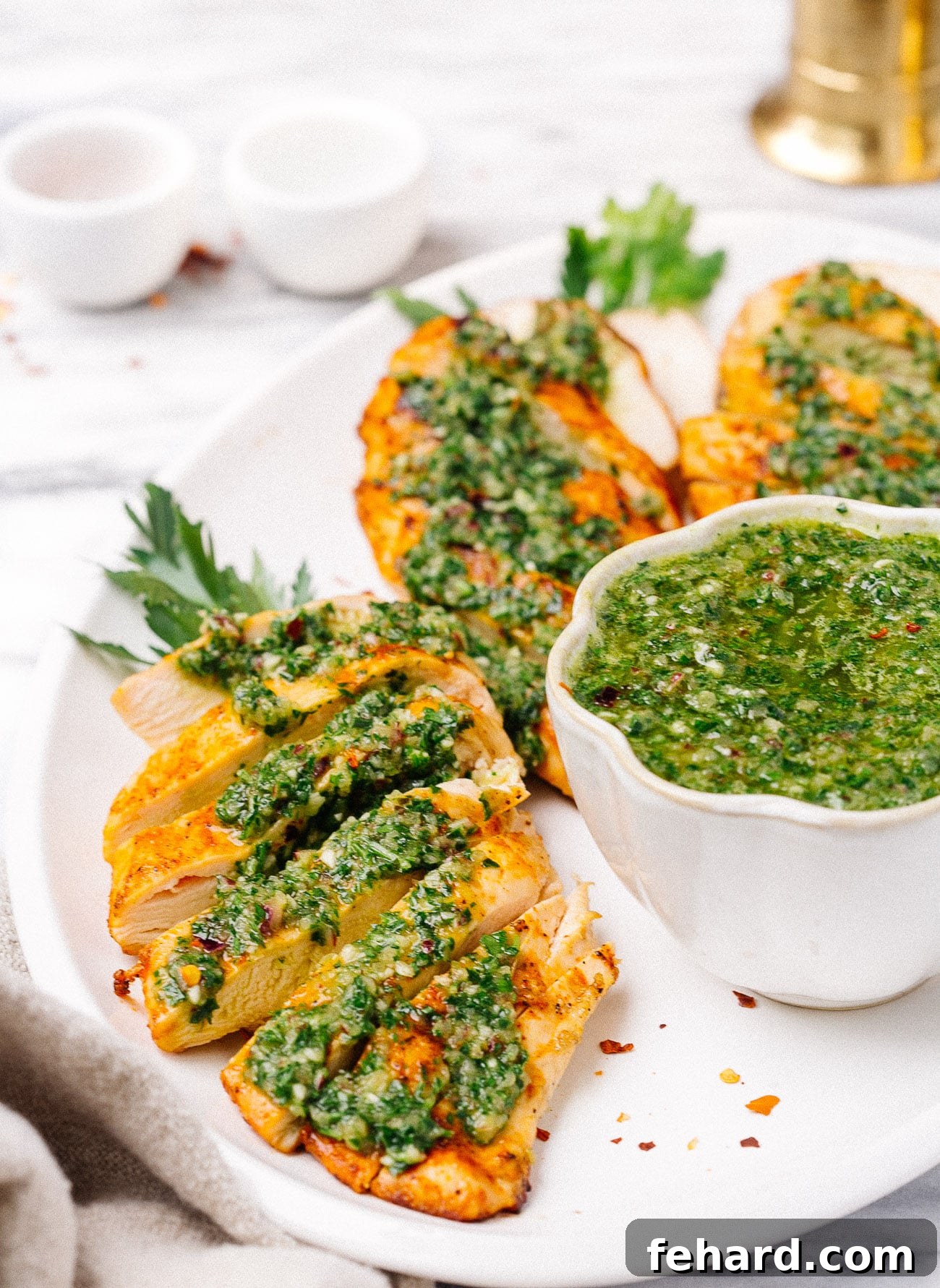 Overhead shot of a full plate featuring grilled chicken breast coated in green chimichurri sauce, highlighting its readiness for consumption.