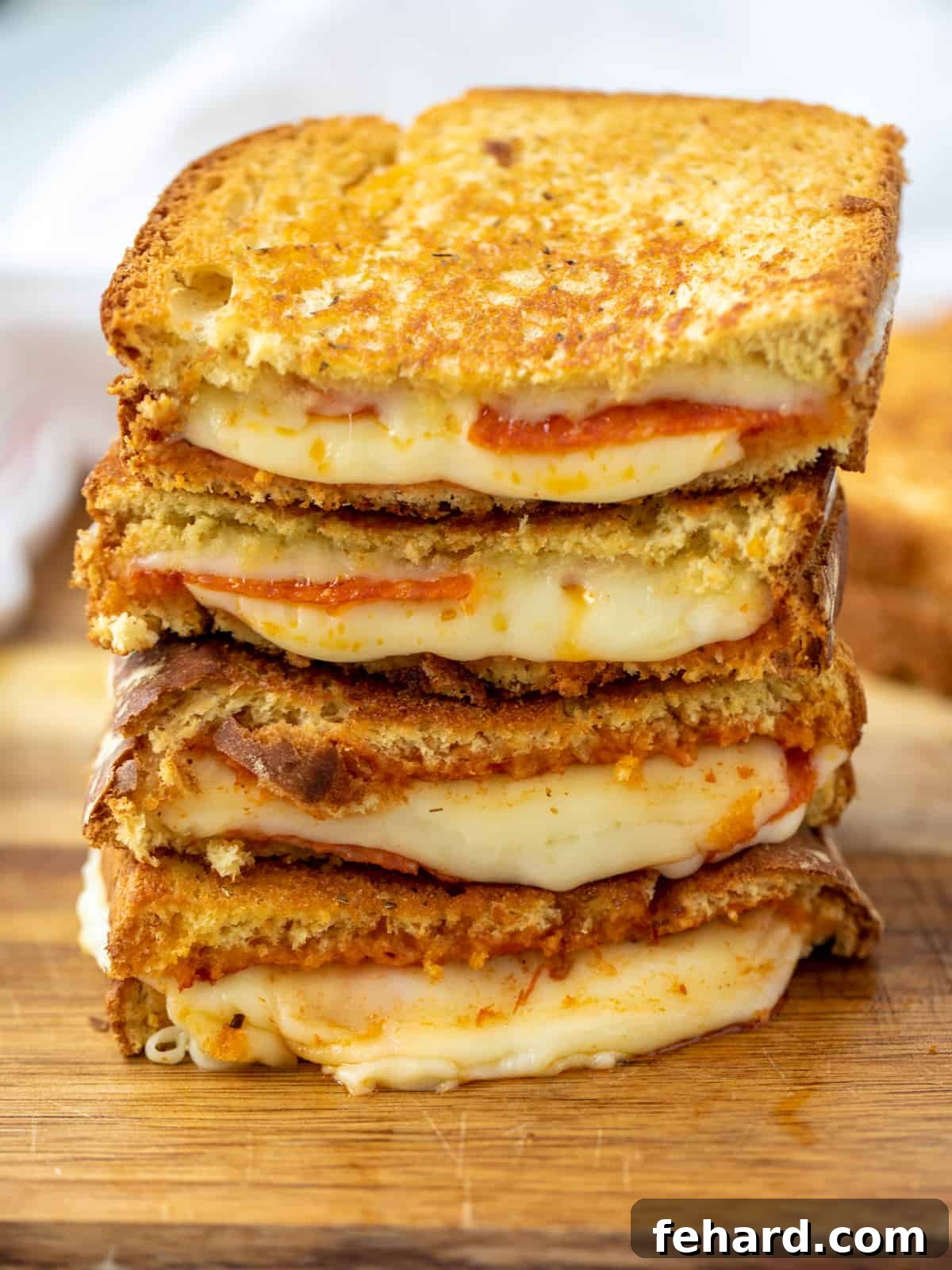 Pizza Grilled Cheese Stack of Pizza Grilled Cheese cut in half showing cheese oozing out on cutting board.