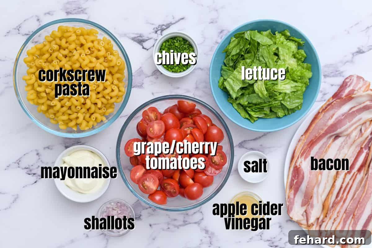 BLT Pasta Salad Recipe Ingredients Labeled ingredients for BLT pasta salad laid out on a kitchen counter, including pasta, bacon, mayonnaise, shallots, vinegar, sugar, salt, chives, tomatoes, and romaine lettuce.