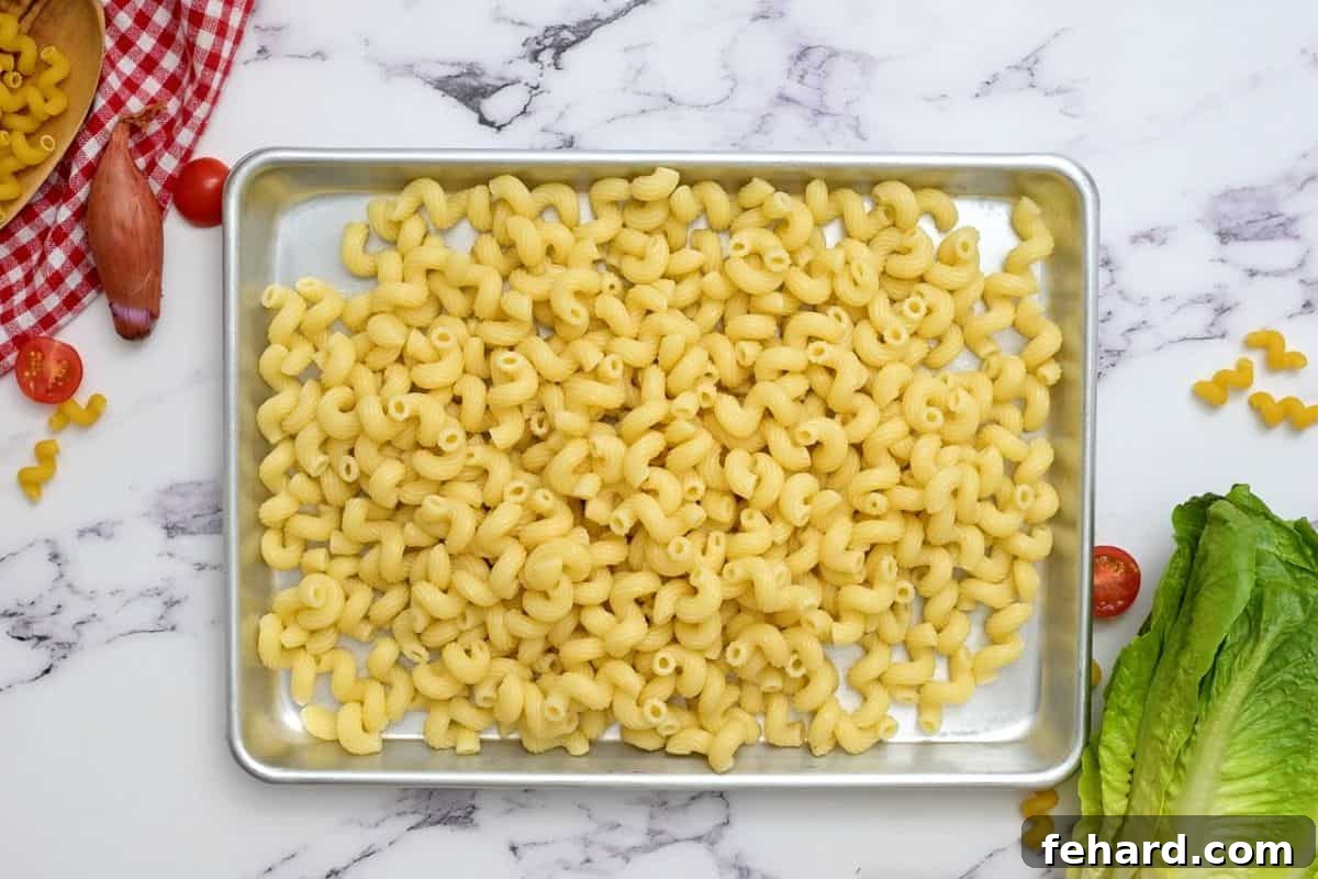 Cooling Pasta for BLT Salad Cooked pasta spread out on a large rimmed sheet pan to cool, with fresh lettuce and grape tomatoes visible nearby.