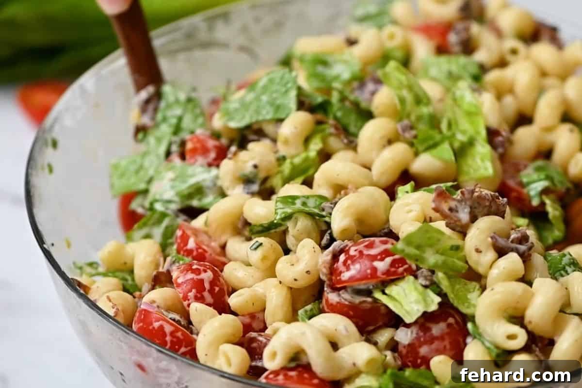 Combining BLT Pasta Salad Ingredients Wooden serving spoons gently tossing together the ingredients for a BLT pasta salad in a large bowl, showing the creamy texture and vibrant colors.