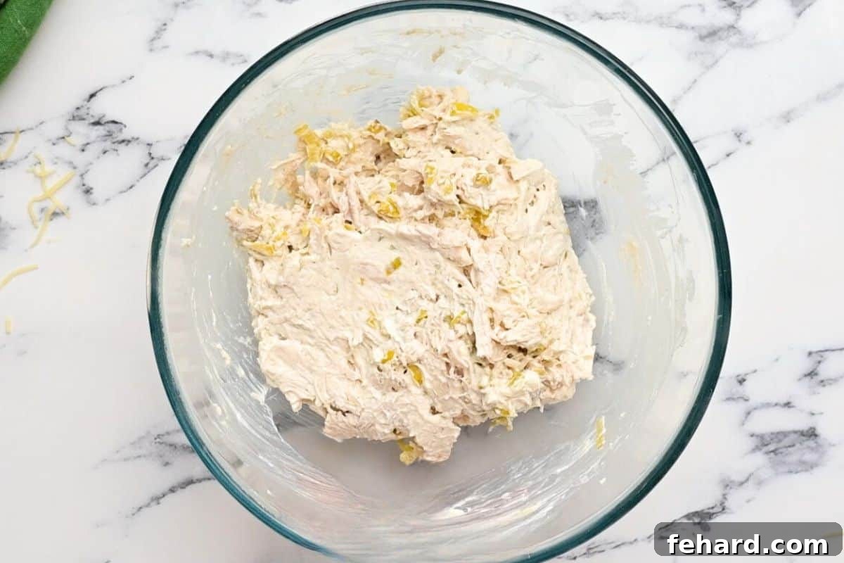 A bowl containing a creamy mixture of chicken, cream cheese, green chiles, and spices, perfectly mixed and ready for assembly.