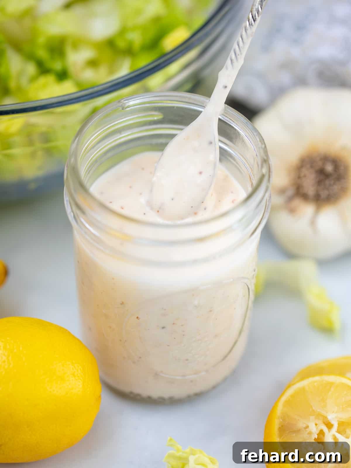 Caesar Salad Dressing Jar of homemade Caesar Salad dressing with spoon next to lemons.