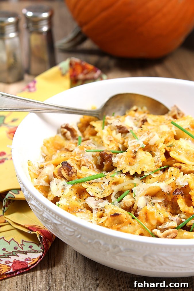 A white bowl featuring bowtie pasta generously coated in a rich pumpkin sauce, adorned with toasted walnuts and fresh chives.
