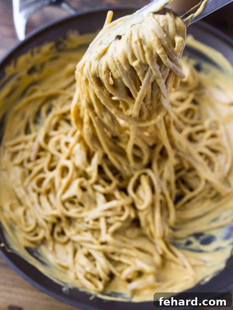 A pair of kitchen tongs gracefully lifting a serving of fettuccine noodles, perfectly coated in a velvety vegan pumpkin sauce.