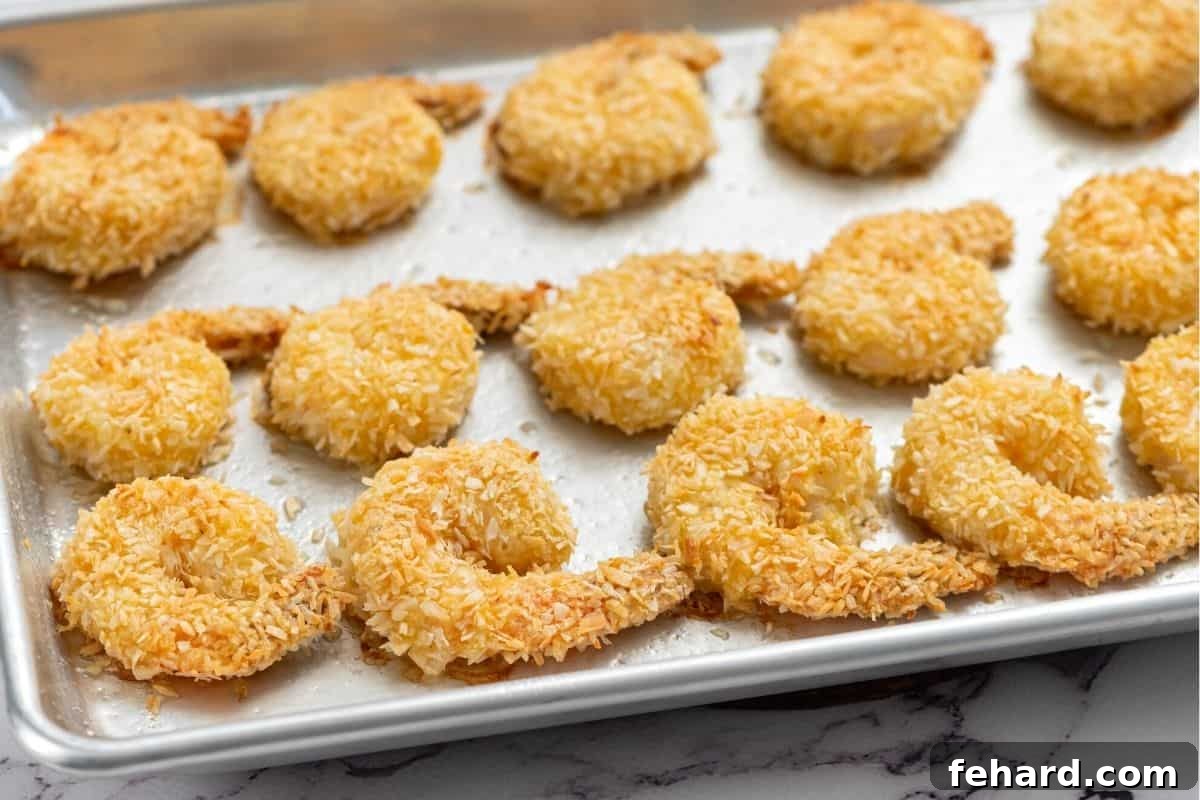 Neatly arranged breaded coconut shrimp on a baking sheet, ready for the oven to become golden and crispy.