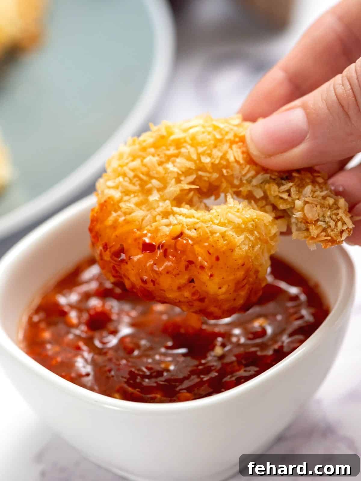 A crispy baked coconut shrimp being dipped into a luscious sweet chili sauce, highlighting its golden exterior.