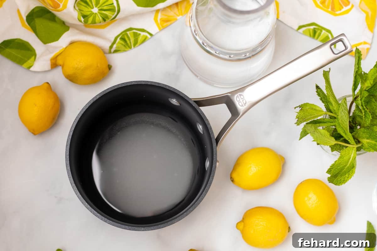 Lemonade with Mint Sugar and water combined in saucepan next to lemons and mint, ready to be heated for simple syrup.