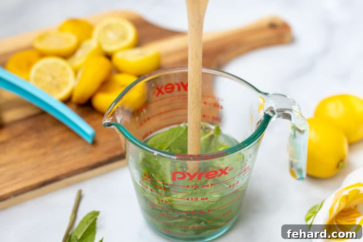 Homemade Mint Lemonade Mint being muddled with wooden spoon in a glass measuring cup filled with simple syrup.