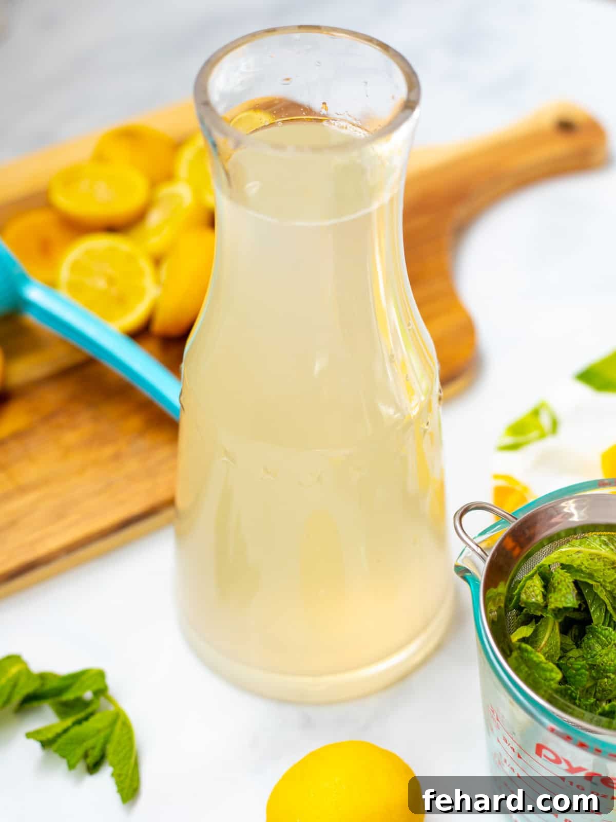 Lemonade with Mint Clear pitcher of mint lemonade next to fresh mint and lemons, ready to be served.