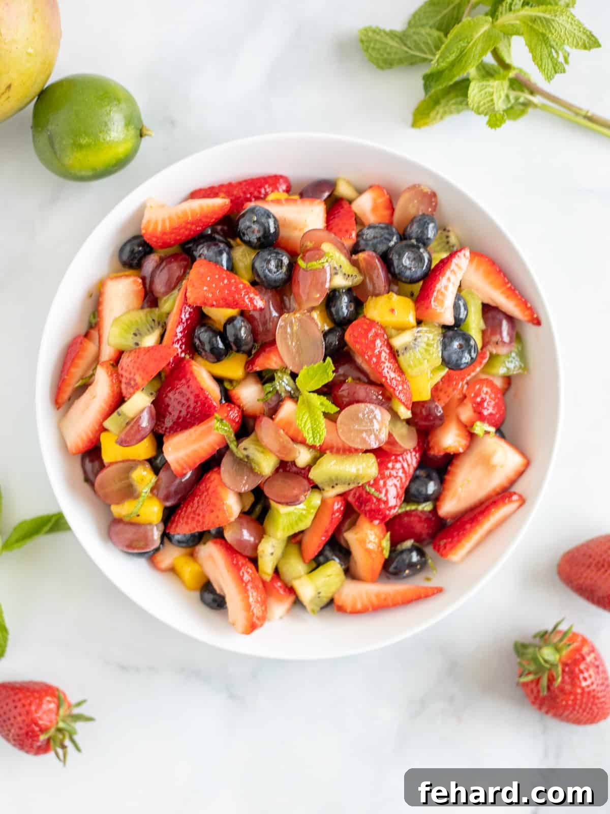 Best Honey Lime Fruit Salad Recipe Bowl of fresh strawberries, blueberries, grapes, kiwi, and mango tossed in a sweet and tangy mint lime dressing.