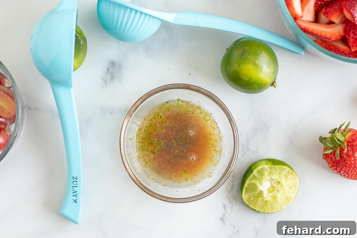 Honey Lime Fruit Salad Dressing Preparation Honey mixed with lime juice and lime zest in small bowl next to fresh fruit for a fruit salad.