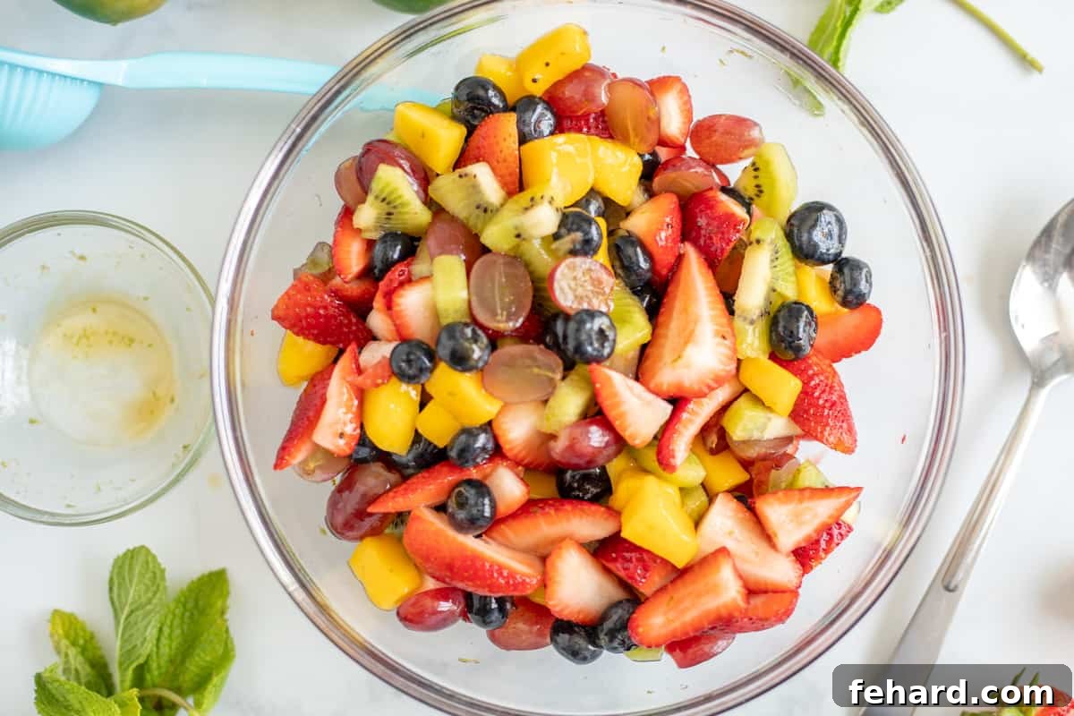Fruit Salad Recipe - Tossing with Dressing Summer fruit tossed with honey lime dressing in a large bowl, ready for chilling.