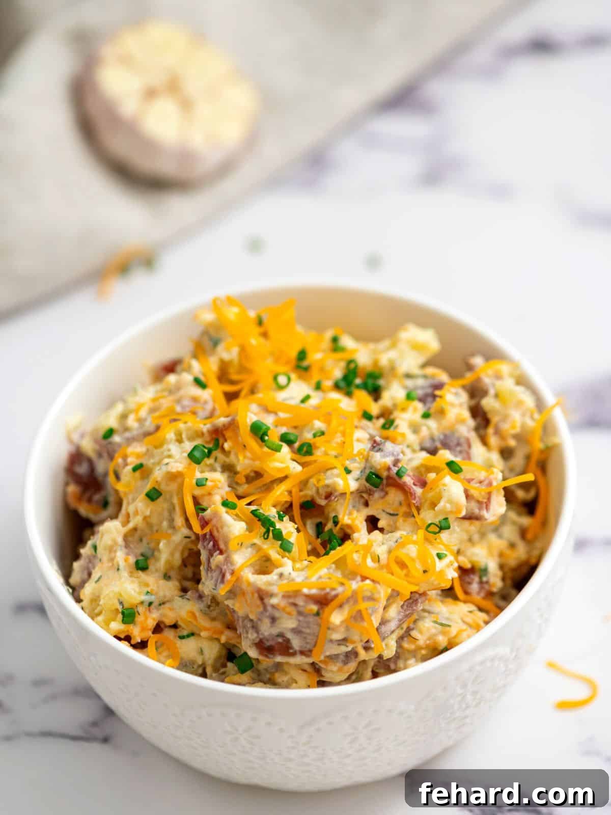 Ranch Potato Salad made with red potatoes and bacon in white serving dish topped with cheddar and chives.
