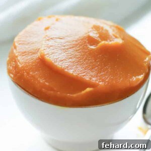 A bowl of vibrant orange homemade pumpkin puree, garnished with a small sage leaf.