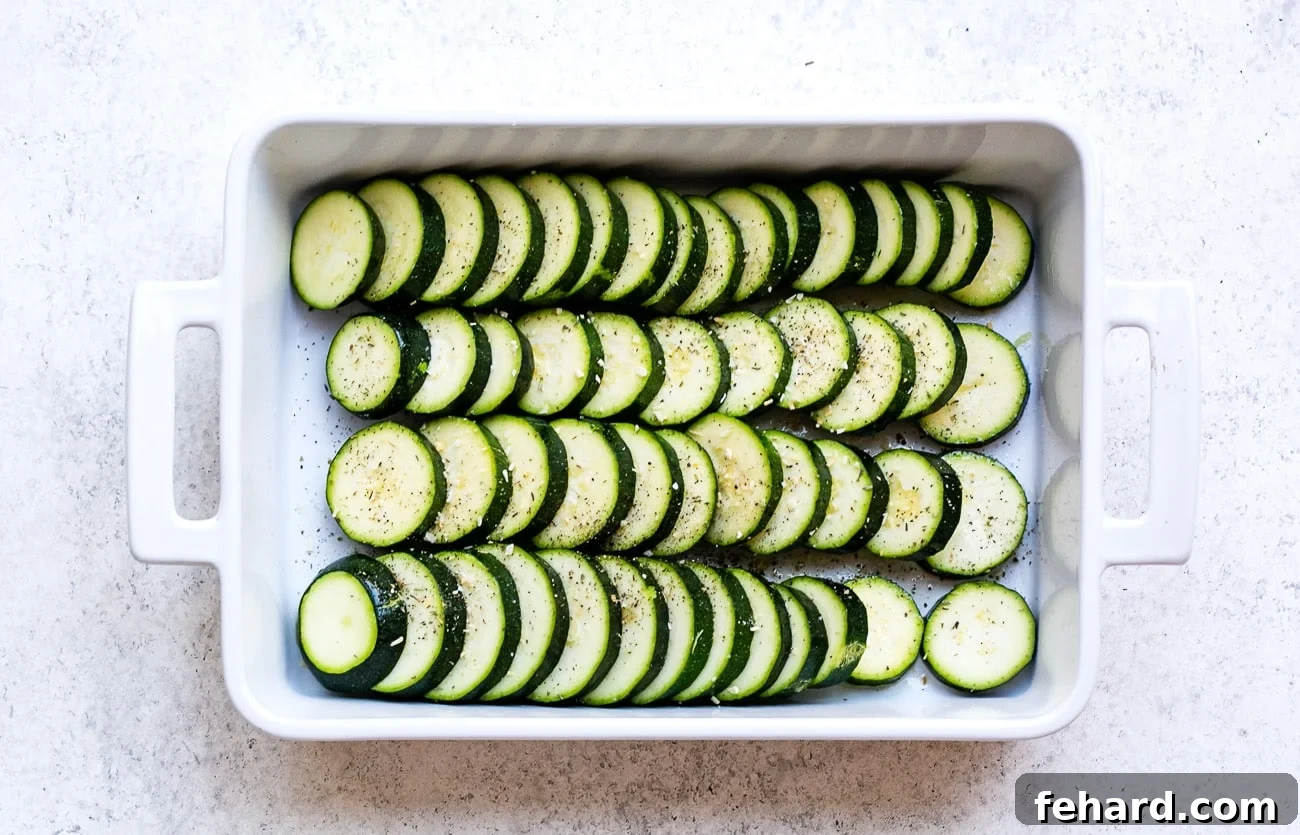 Golden Zucchini Gratin 4 Slices of zucchini arranged in baking dish. Slices are seasoned with salt and pepper.