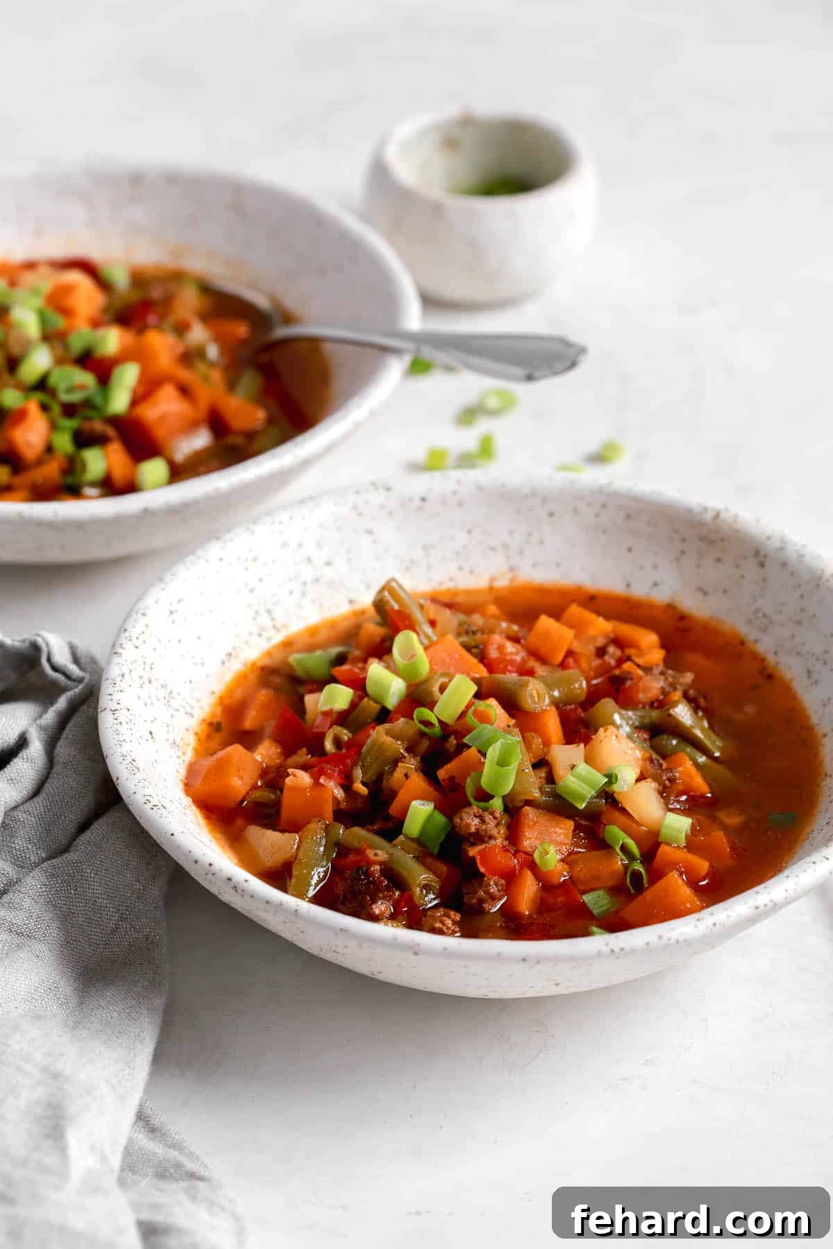 Two bowls of freshly made beef vegetable soup cooling on a kitchen counter, ready for serving.