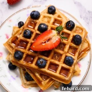 Three whole wheat waffles on white plate topped with berries and maple syrup.