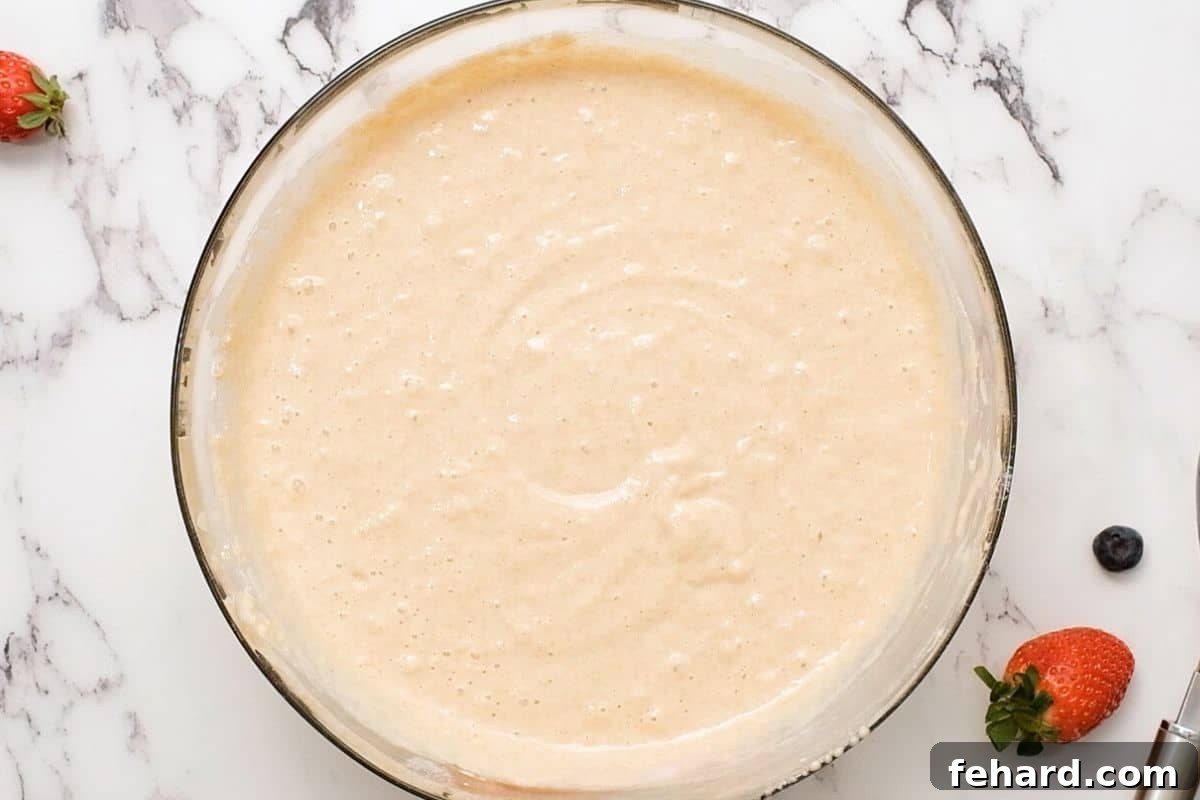 Homemade Whole Wheat Waffle Batter Smooth waffle batter being whisked together in a large stainless steel mixing bowl, ready for cooking.
