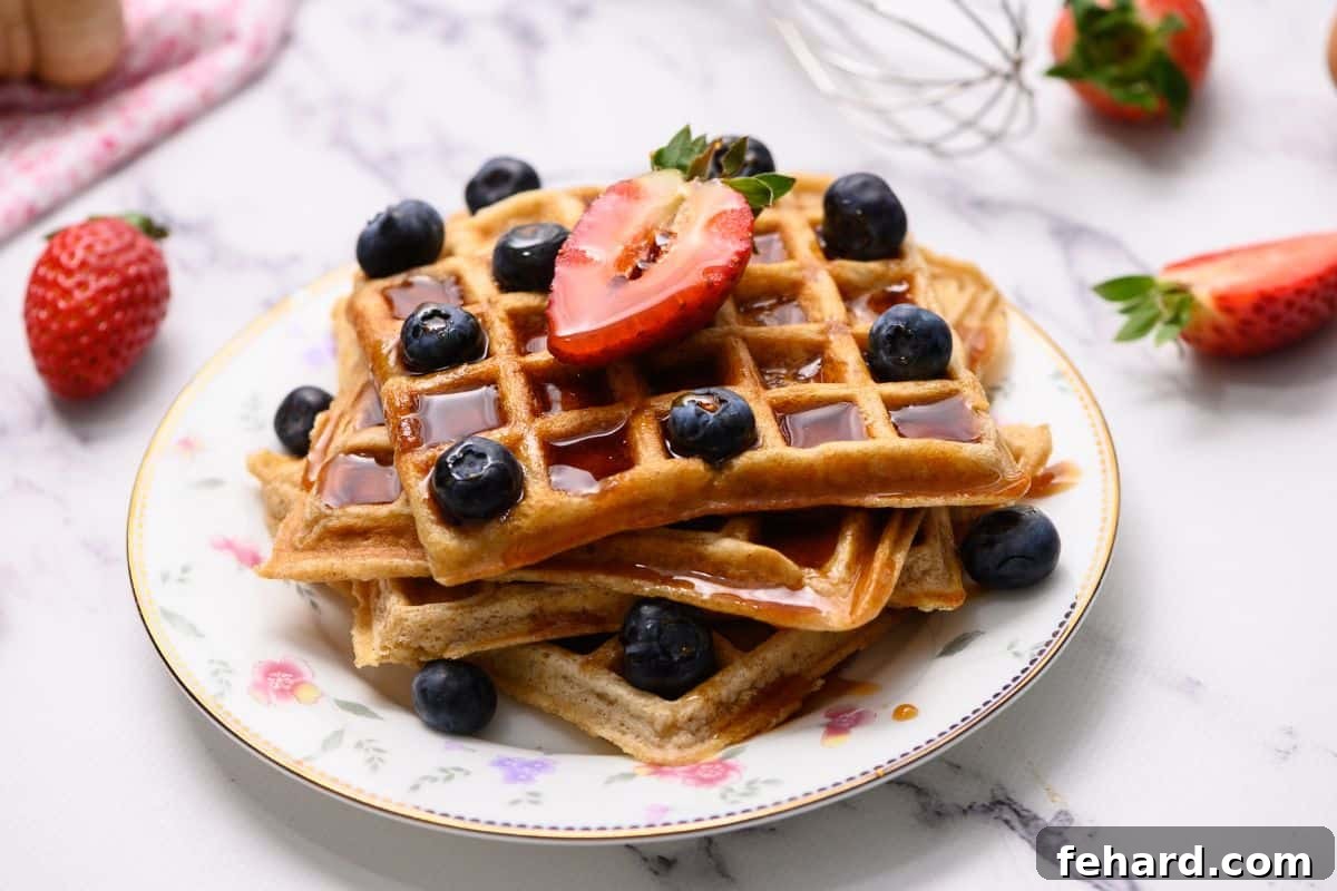 Beautiful Whole Wheat Waffle Recipe Presentation Three whole wheat waffles artfully arranged on a white plate, garnished with fresh berries and a golden stream of maple syrup.