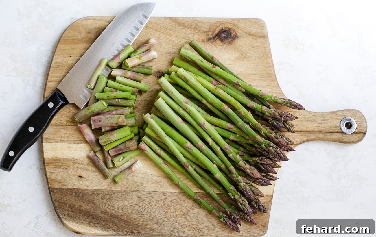 Golden Asparagus Gratin 4 Hands cutting woody ends from asparagus on a cutting board.