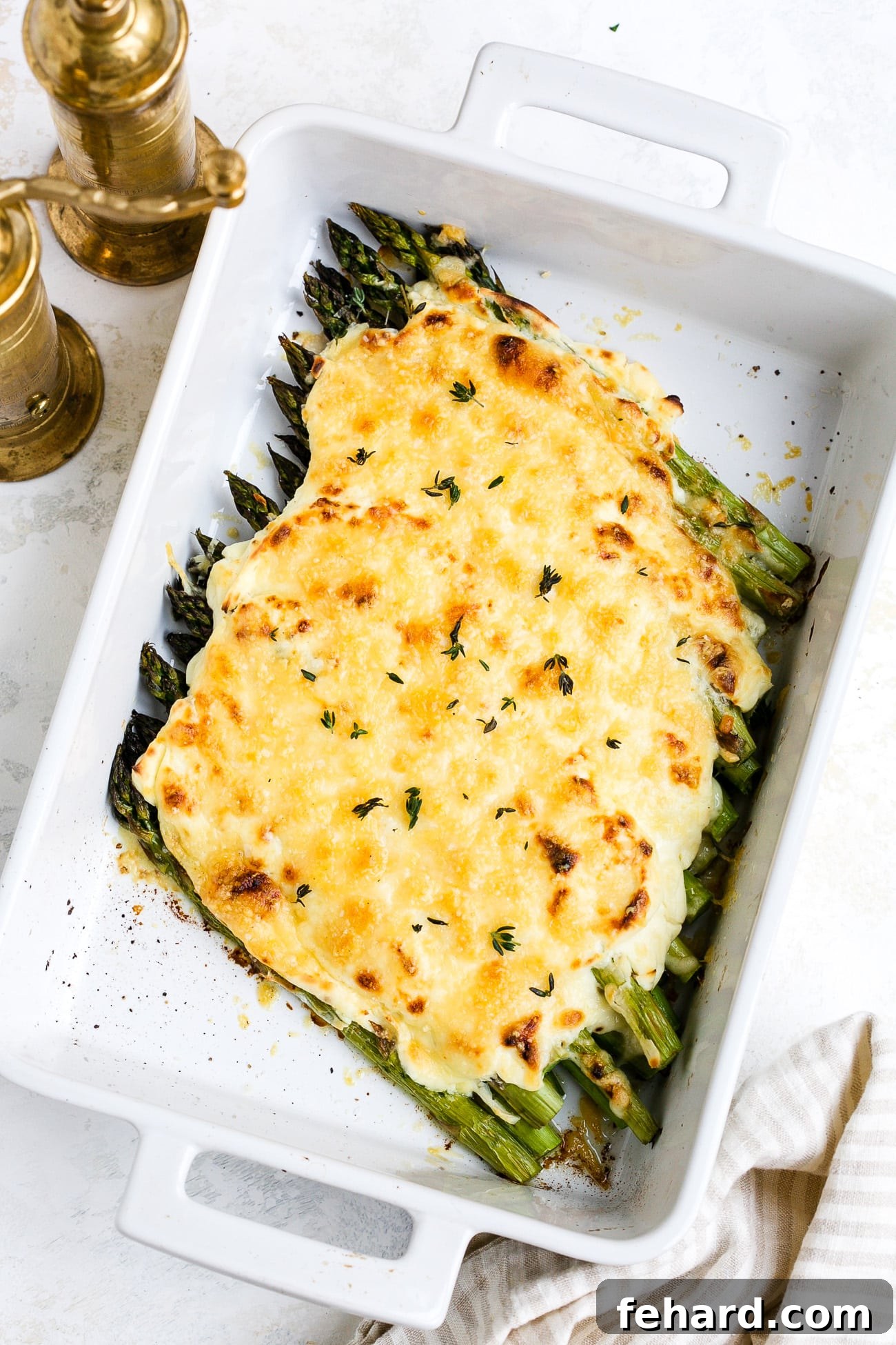 Golden Asparagus Gratin 7 The finished cheesy asparagus casserole in a white baking dish, garnished with fresh parsley.
