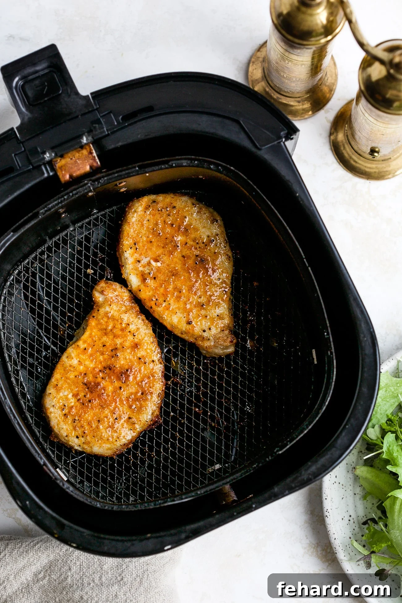 Golden Crispy Air Fryer Pork Chops 2 Cooked pork chops, golden brown and crispy, perfectly arranged in an air fryer basket.