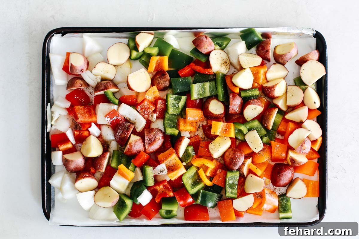 Colorful chopped bell peppers, potatoes, and onions on a baking sheet, ready for roasting.