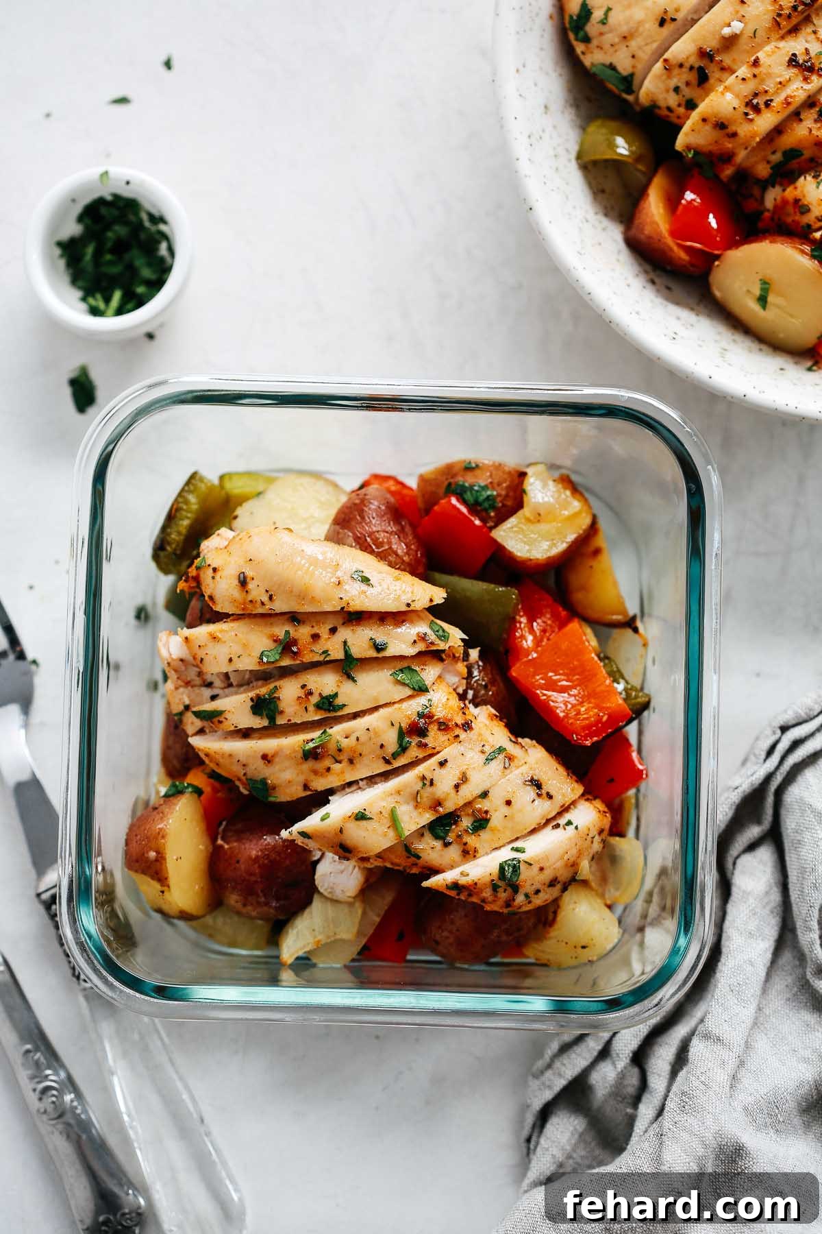 Slices of perfectly roasted chicken breast alongside roasted vegetables in a square meal prep container.