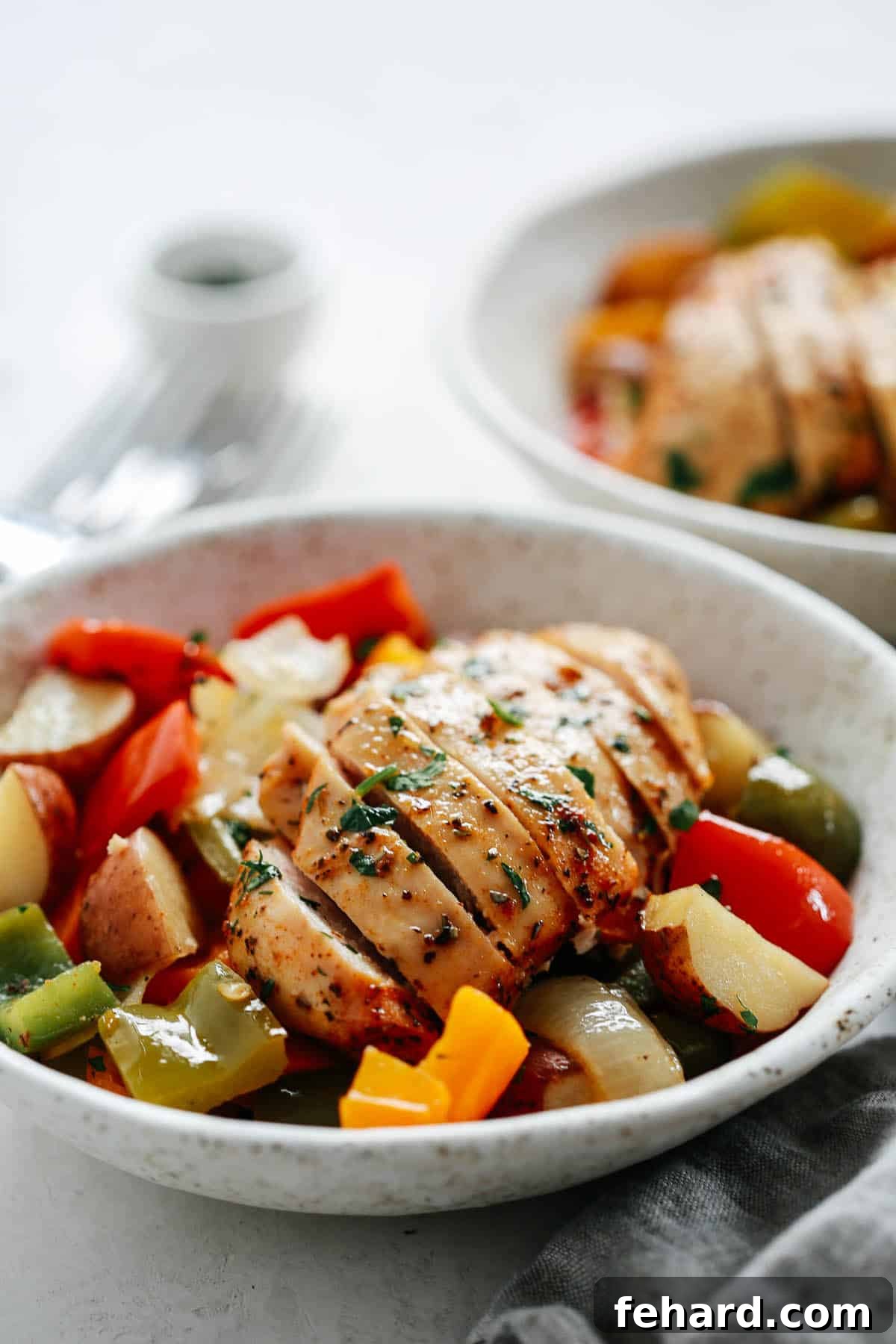 Beautifully plated roasted chicken and vegetables, garnished with fresh herbs, on a white dinner plate.