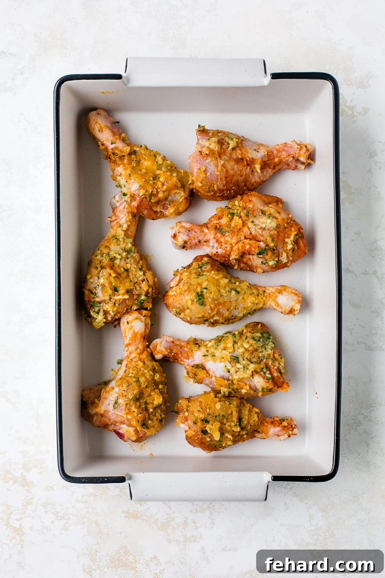 Irresistible Garlic Butter Chicken Legs 6 Unbaked, seasoned drumsticks lined in a baking dish.