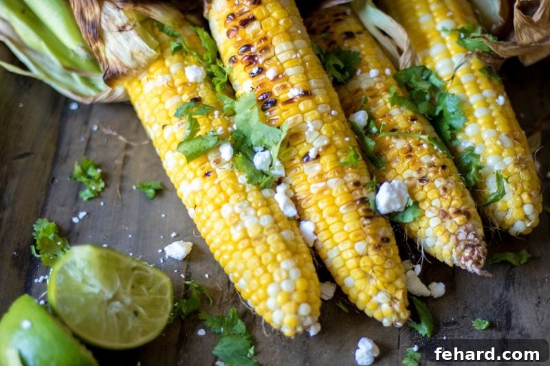 Mexican Grilled Corn on the Cob Two ears of Mexican street corn (Elote style) on a rustic wooden platter, topped with mayonnaise, chili powder, cilantro, and cotija cheese.
