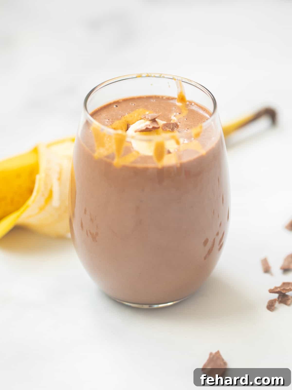 A vibrant Chocolate Peanut Butter Protein Smoothie in a clear glass, beautifully garnished with slices of banana, a generous drizzle of creamy peanut butter, and delicate chocolate shavings on top, set against a bright, inviting background.