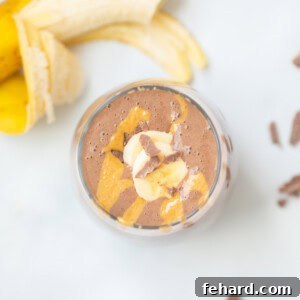 Top-down view of a chocolate peanut butter smoothie in a glass, topped with peanut butter, chocolate pieces, and sliced banana.